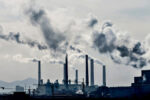 Industrial facility with multiple smokestacks emitting thick clouds of smoke, representing pollution and environmental impact.