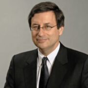 Headshot of a person wearing glasses and a suit with a tie, set against a plain background.