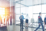 Businesspeople in a modern office setting with cityscape reflections. The scene conveys professionalism and corporate activity.