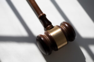 A wooden gavel with a brass band, symbolizing justice or legal proceedings, casting a shadow on a white surface.