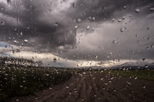 Rainy Storm Raindrops on a window with a view of a dark, cloudy sky and a landscape, representing a stormy or rainy weather scene.