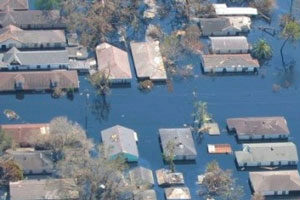 Floodhouses Aerial view of a flooded neighborhood with numerous homes partially submerged in water. Trees and debris are visible, indicating a natural disaster.