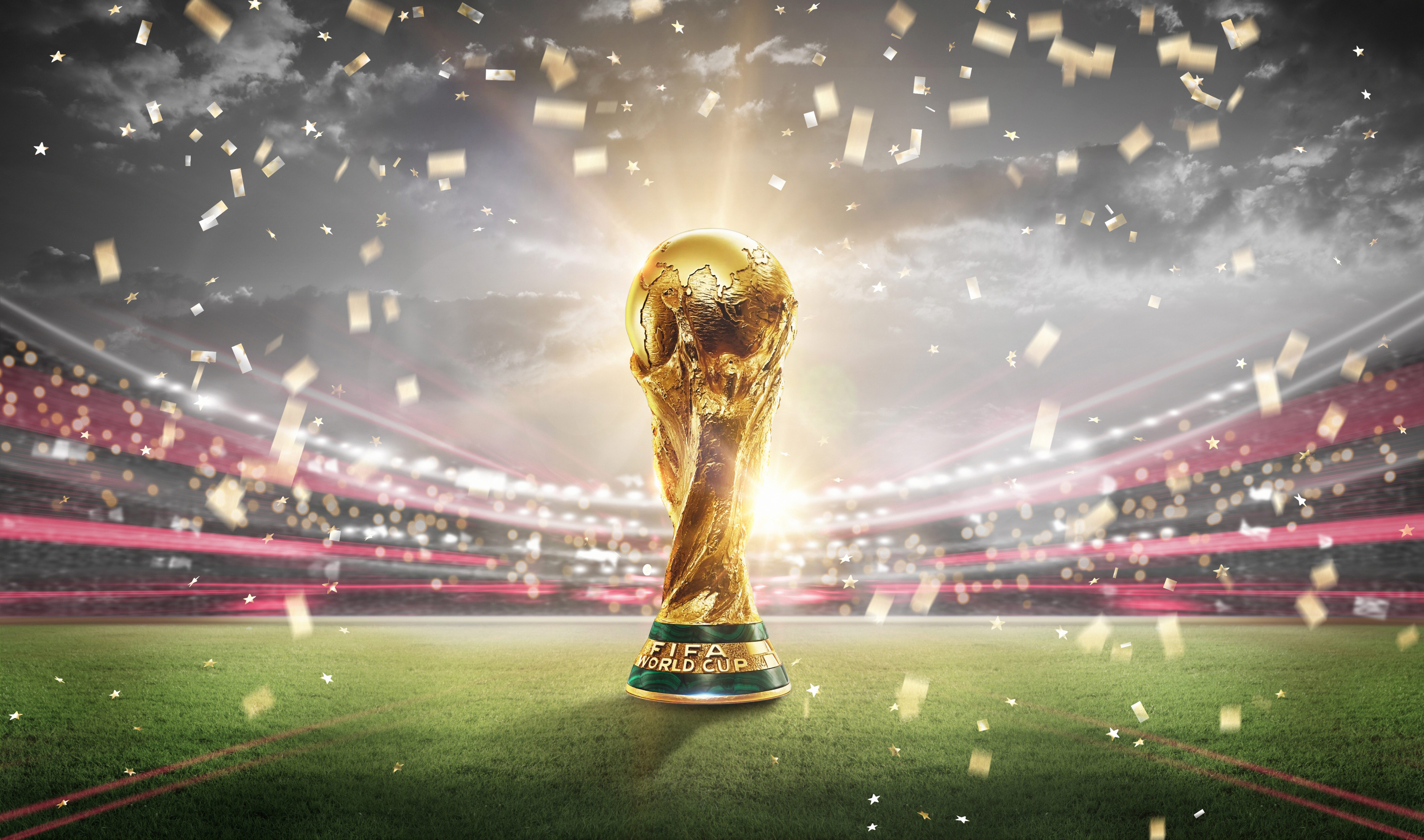 Stock image of FIFA World Cup 2022 trophy sitting on grass in stadium surrounded by confetti