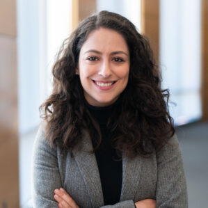 Woman smiling in black turtleneck and grey blazer with arms crossed