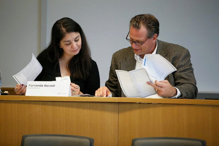 Two individuals are seated at a desk, reviewing and discussing printed documents together, suggesting a collaborative or professional work environment.