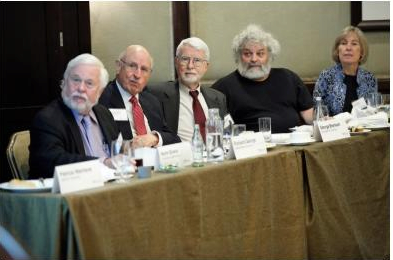 Five people seated at a conference table, with name tags and papers in front of them, appearing engaged in a discussion or meeting.