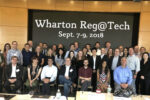 A group of people posing for a photo in front of a sign that reads "Wharton Reg@Tech Sept. 7-9, 2018." They appear to be at a conference or event.