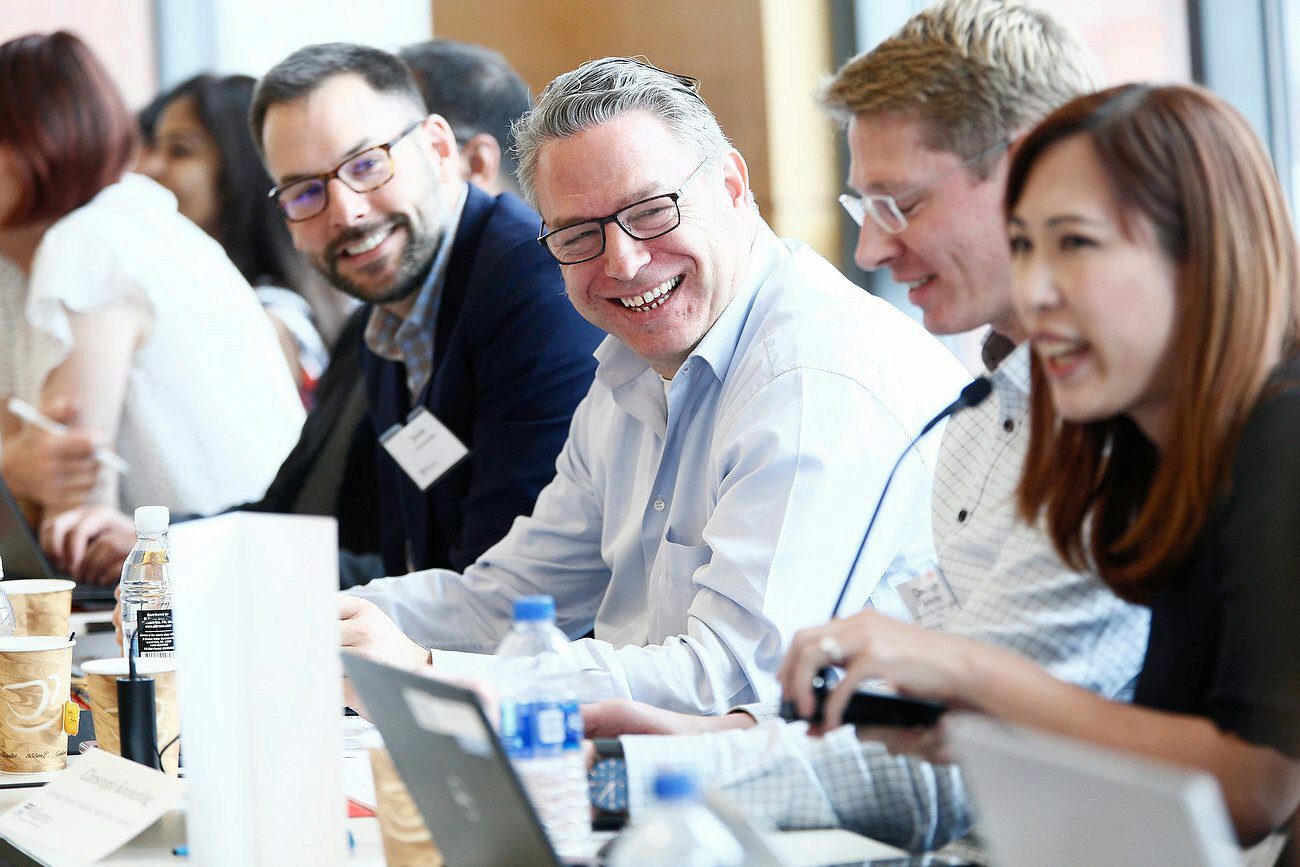 A group of people sitting at a conference table, engaged in a lively discussion. They are smiling and appear to be enjoying the conversation.