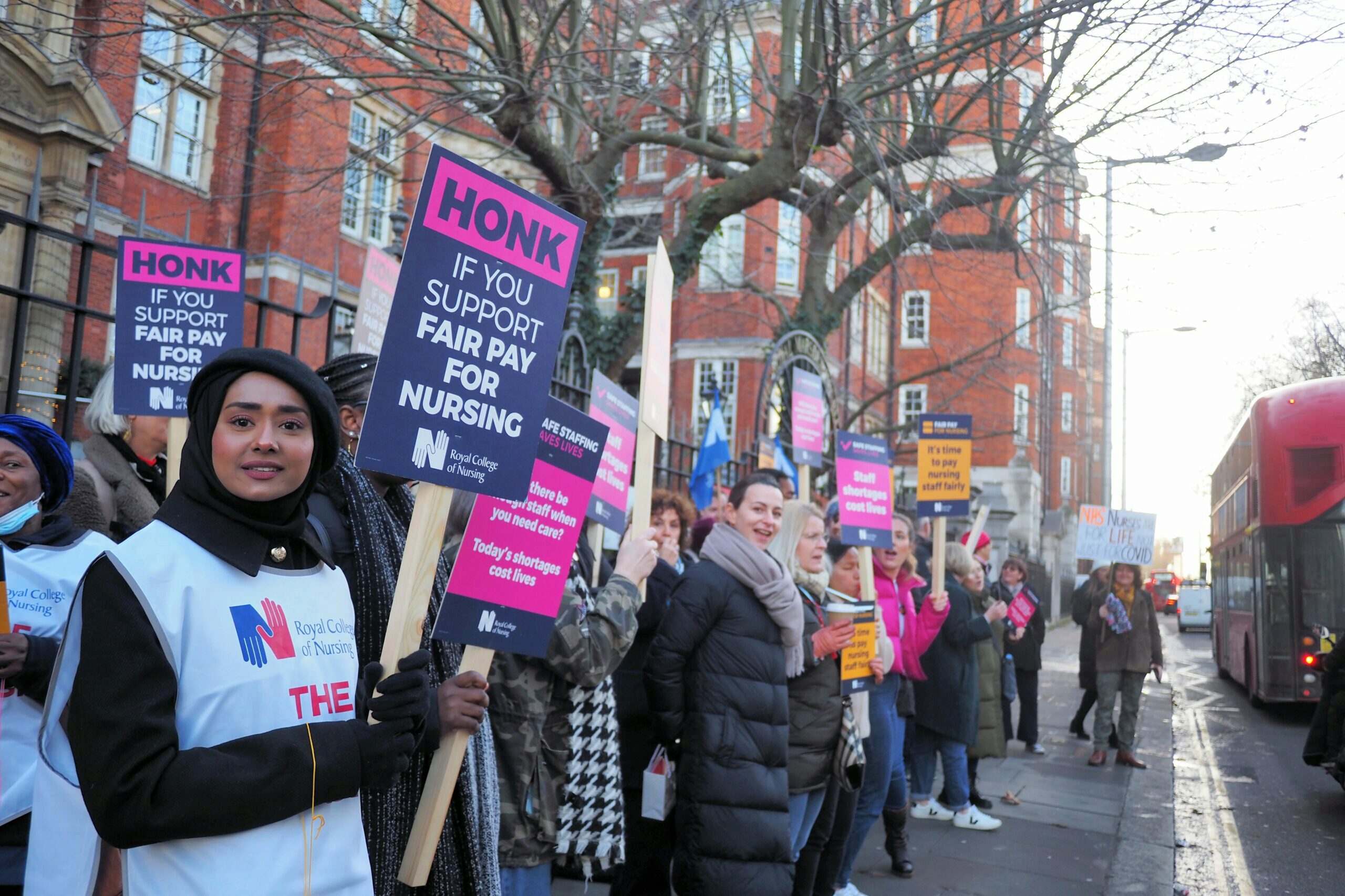 Photo of nurses on strike on the streets of London. Signs are visible that say "honk if you support air pay for nursing"