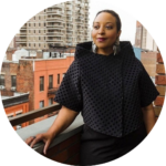 Gayle Jennings O'Byrne smiles and looks into distance in black top in front of a city scape with red brick buildings