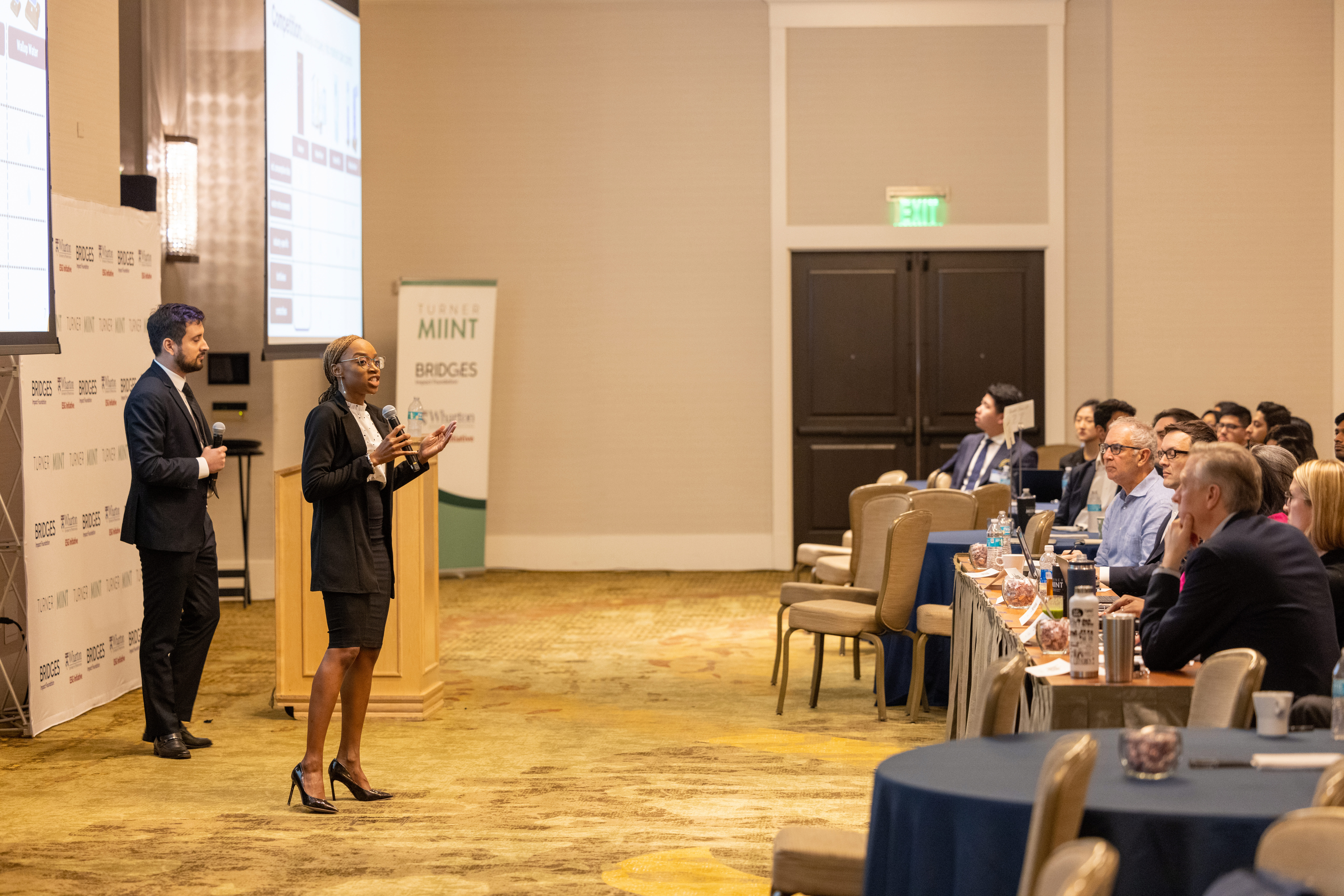 2023 TMIINT Student Finals Students at the front of a ballroom pitching a company to a panel fo judges and group of peers.