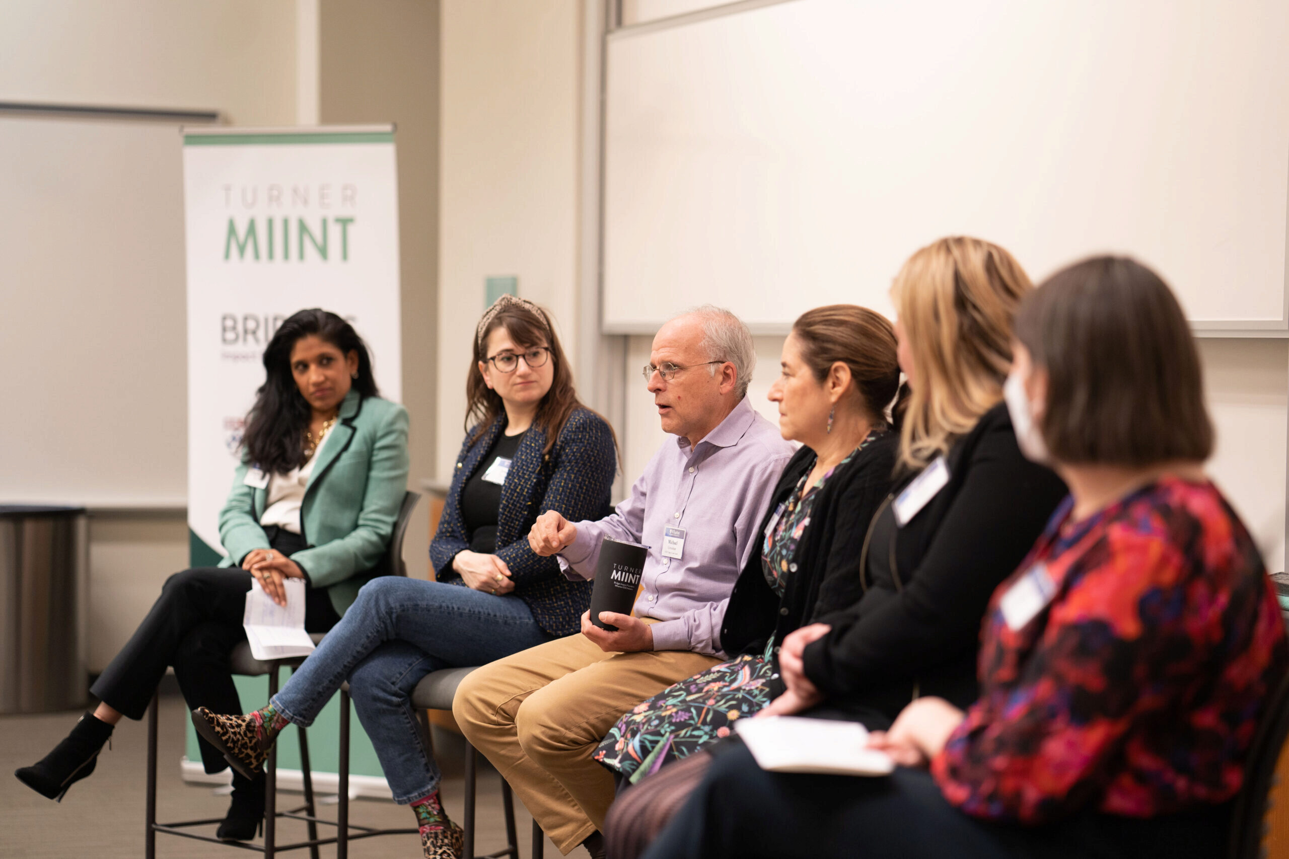 Lunchtime career panelists in impact investing and ESG sit at the front of a classroom in a row of high chairs.