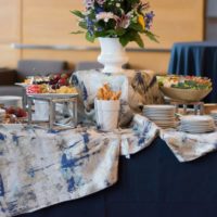 A buffet table with various appetizers, including fruit and breadsticks, decorated with a floral centerpiece.