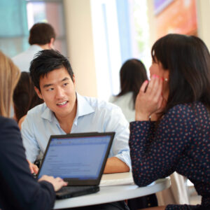 MBACM Students and Recruiters 2015 Students talking indoors around a round table with laptops open