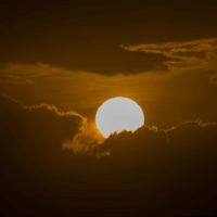 A sun partially obscured by dark clouds, creating a dramatic sunset or sunrise scene.