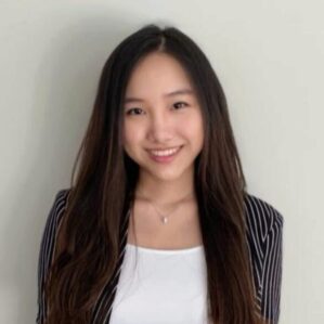 Sapphira Ching Headshot Sapphira Ching smiling in a black and white pin stripe blazer and a white shirt against a white wall