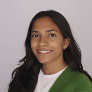 Maithili Kamble smiles into the camera, wearing a white shirt and green sweater against a neutral backdrop.