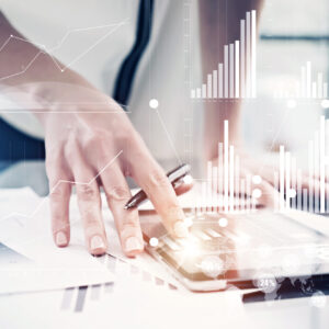 Picture,Female,Hand,Touching,Modern,Tablet.investment,Manager,Working,New,Private A hand holding a pen hovers above a tablet set on a table surrounded by papers with graphs on them. Person in background wears a white shirt and blue tie and blue pants, standing in front of a window. Graphs are overlaid over the image.