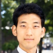 Jisung P Headshot of a person with short, dark hair, wearing a suit, standing outdoors with blurred greenery in the background.