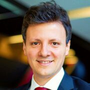 Leandro P Headshot of a person with short dark hair, wearing a suit and red tie, smiling, with a blurred background.
