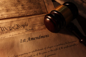 First,Amendment,And,Us,Constitution,Text,With,Legal,Gavel A gavel sits atop a sheaf of papers; the top paper is the first amendment, with a sepia filter.