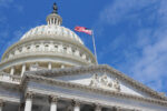 The capitol building from below with the sky in the background and an American flag.