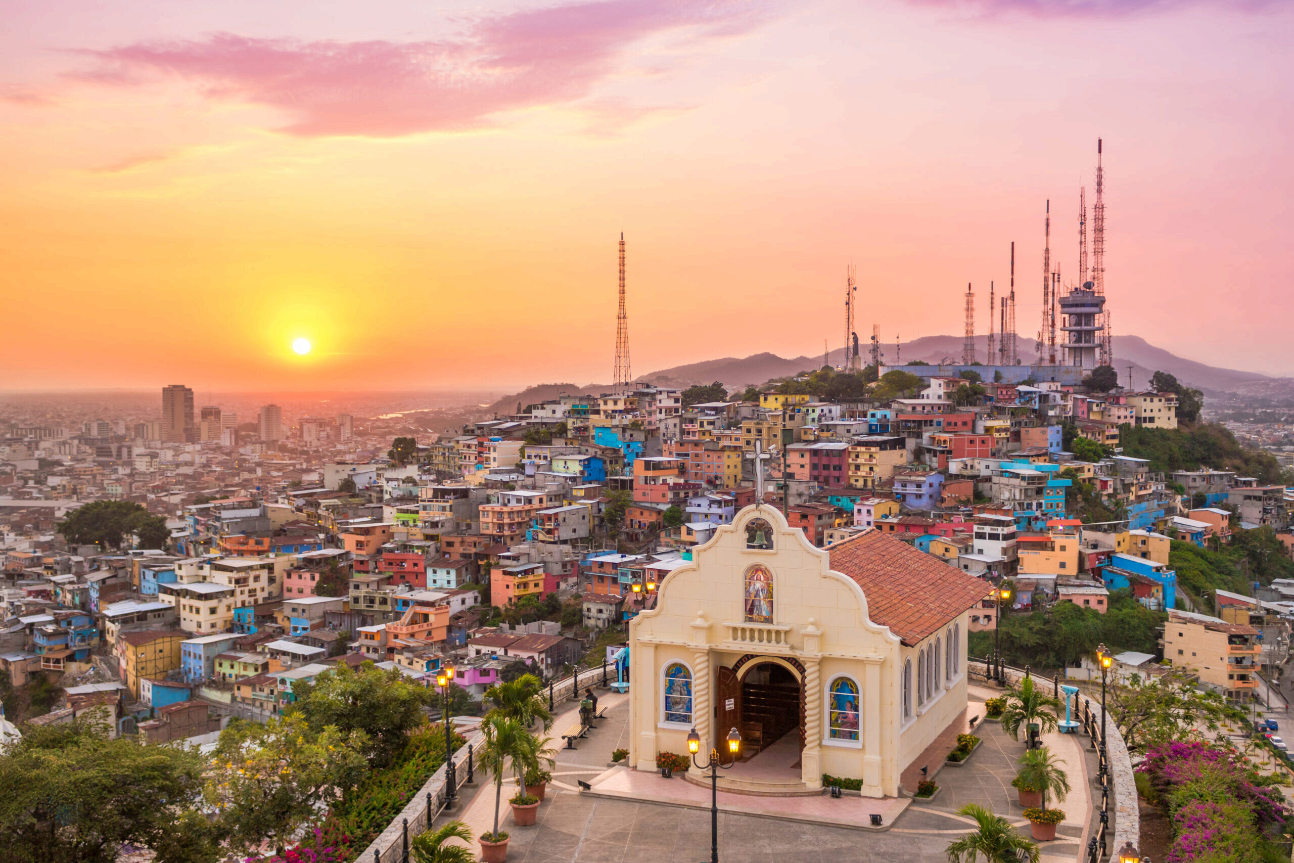 Sunset In The City Of Guayaquil Decorative image of Sunset In The City Of Guayaquil with an old church in the foreground and colorful homes on a hill in the background