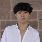 Headshot Ray Liu Photo of Raymond Liu Ao smiling towards the camera in a white button down shirt in from of a stone wall