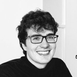 Black and white headshot of a smiling person with curly hair and glasses.