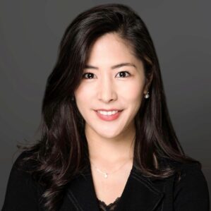 Ai Yamakami smiles in a black blazer in front of a dark grey backfrop.