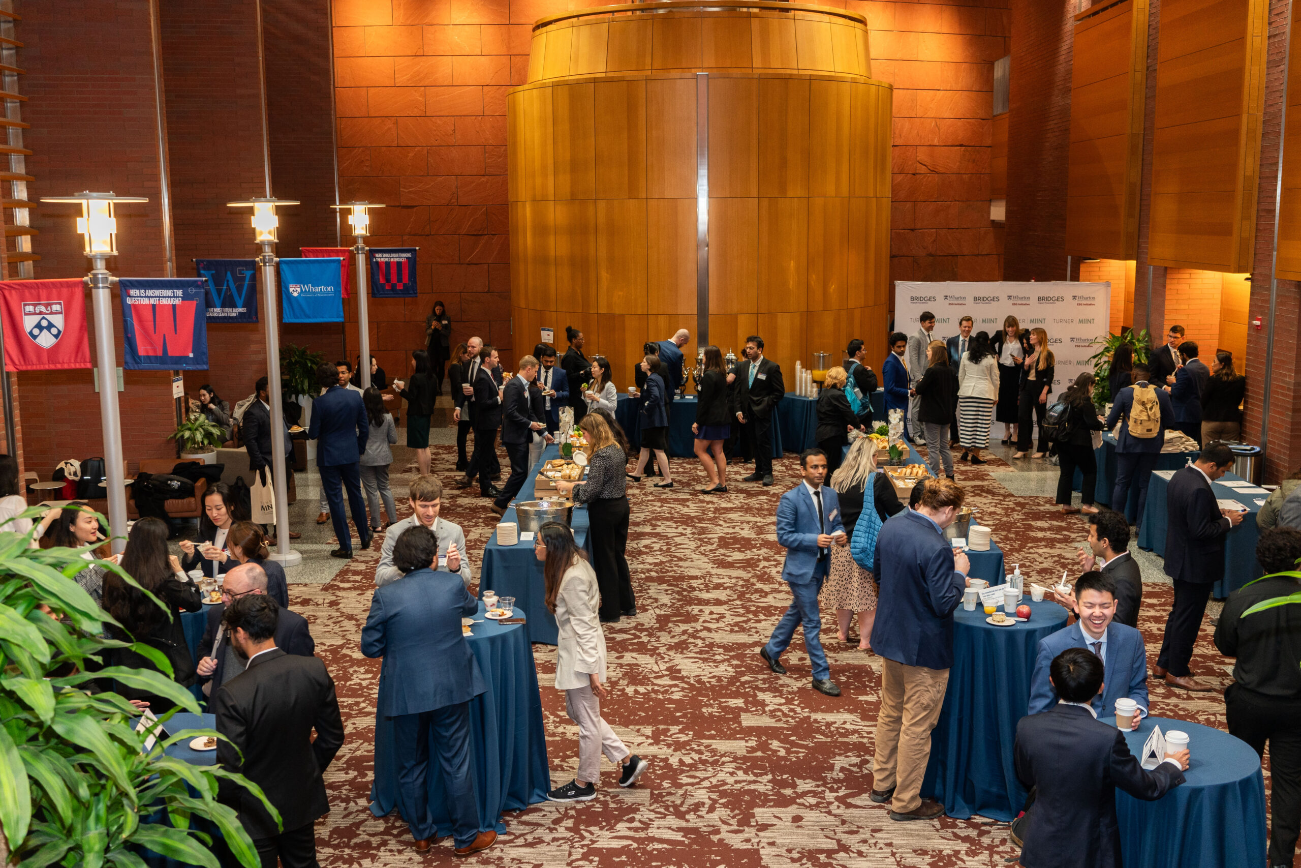 The forum on Huntsman Hall full of students in business casual attire networking and eating breakfast at high top tables.