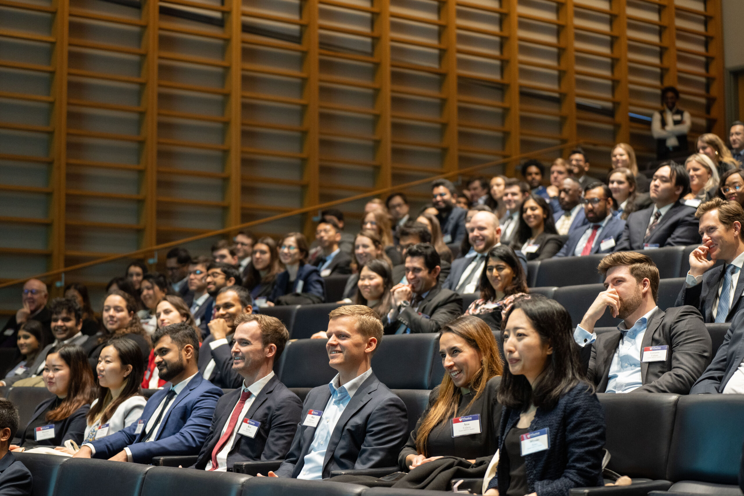 Wide shot of students seated in a lecture hall listening to a speaker.