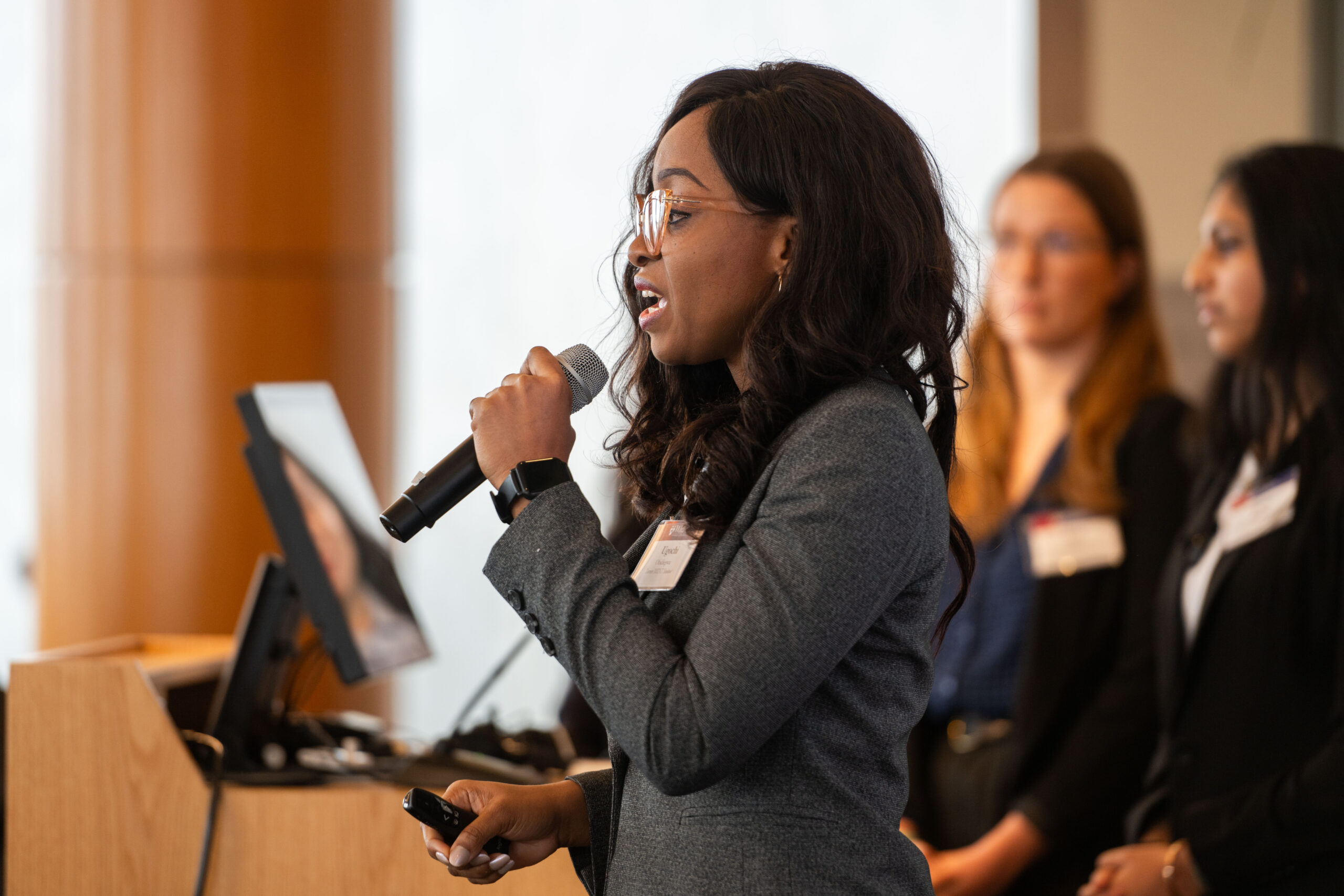 Close up photo of a student in business casual attire presenting into a microphone.