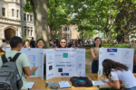 Students hold up posters outside in front of trees.