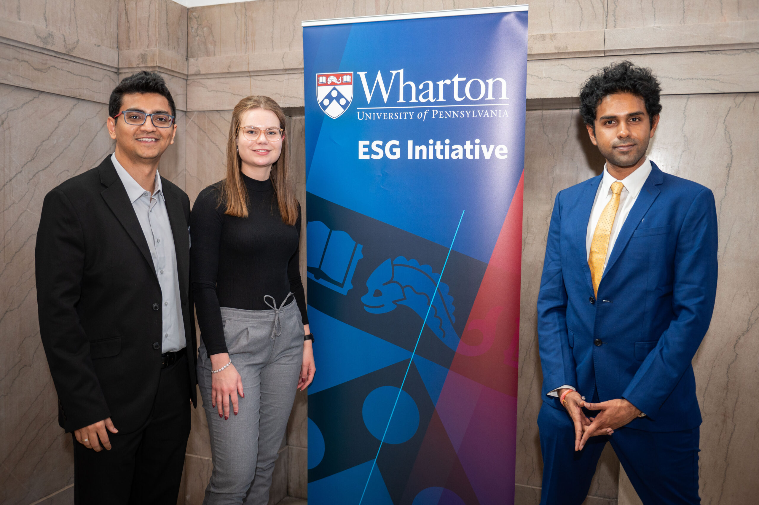Fletcher School At Tufts University TIPC 2024 Three members of the Fletcher School at Tufts University team pose in professional attire next to a banner that reads "Wharton ESG Initiative"