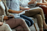 Five people sit cross legged holding papers and laptops.