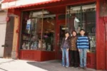 A small group of people standing in front of a storefront with a red facade and large windows displaying various items.