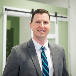 Garrison Haning smiles in a white button down, blue patterned tie, and grey suit jacket.