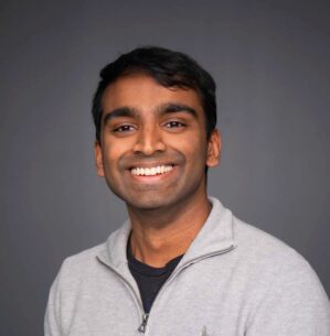 Rupesh Jayaram poses for a professional headshot in a grey quarterzip.