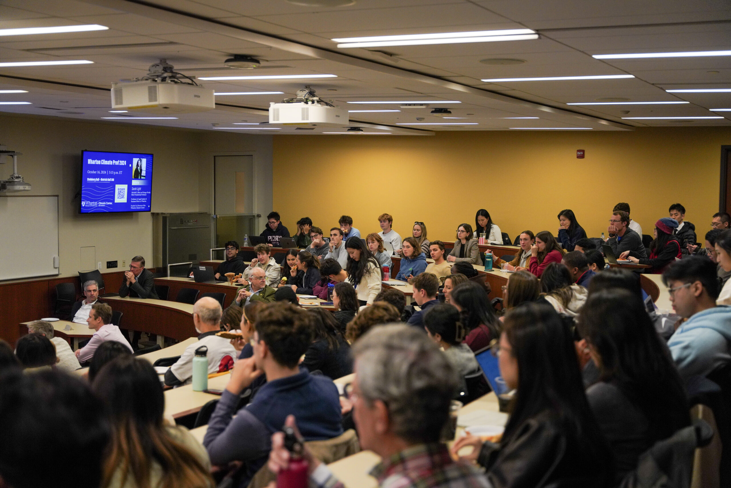 Photo taken from the back of a packed classroom of people watching a presentation