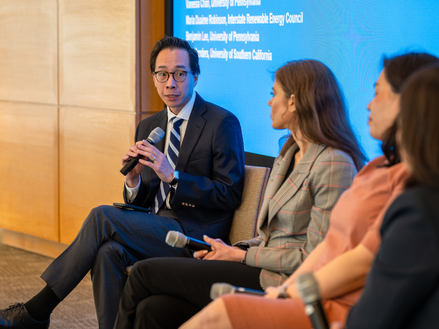 Three panelists speak holding microphones